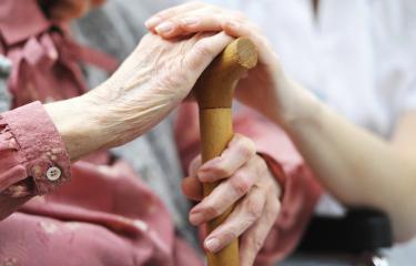 Elderly hands hold a wooden cane