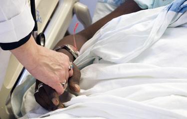 A care giver holds the hand of a patient in a comforting way